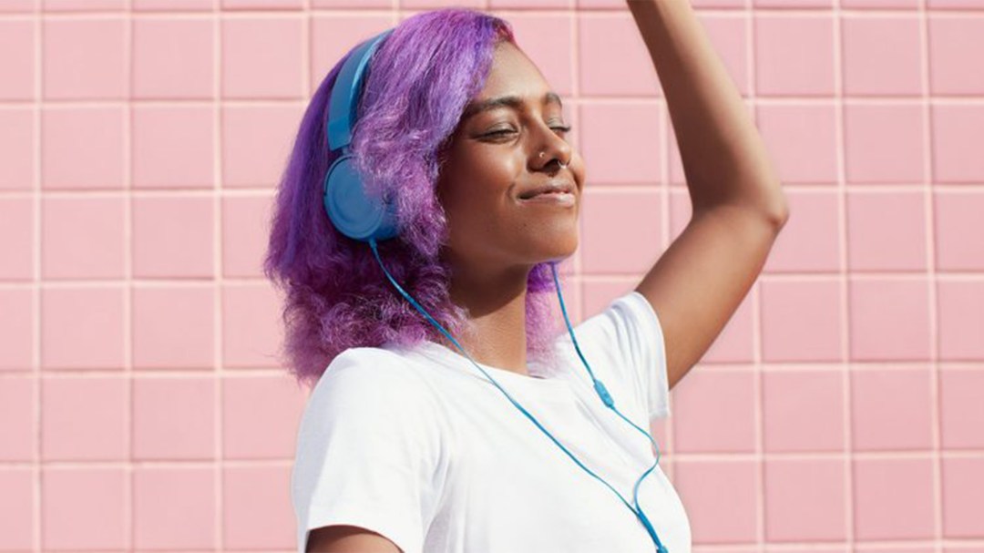 A young lady with pink hair enjoys some music over headphones