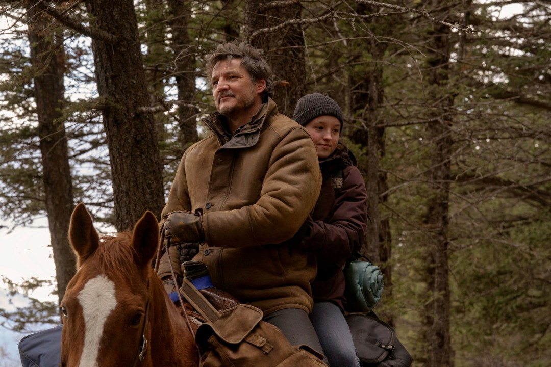 Joel and Ellie from The Last of Us on horseback in a forest.