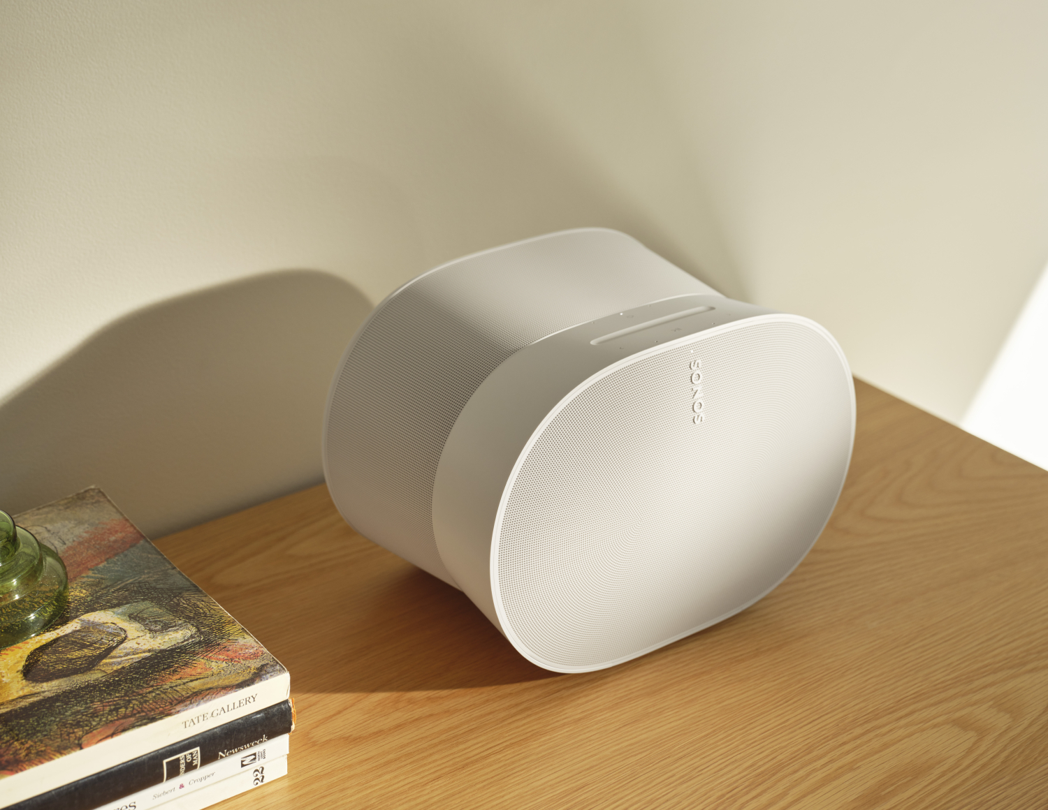 A Sonos 300 speaker in white next to a pile of books.