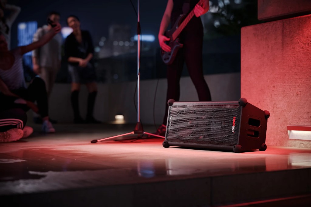 A Sharp SumoBox on stage with a person playing guitar behind it.